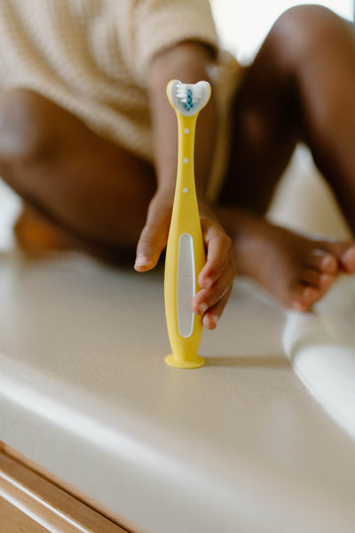 Frida Baby Training Toothbrush | Toddler Toothbrush for 18-24 Months, Easy-Grip Handle, Triple Angle Bristles, Soft Toothbrush Bristles, Stay-Put Suction Cup | Yellow